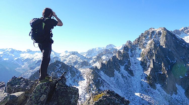 Un homme prend un photographie, sur une crête de montagne enneigées. 
